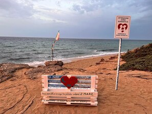 A beach with a wooden sign with multiple messages, a flag, and a warning sign. - Apartment in beachfront residence (Campomarino di Maruggio)