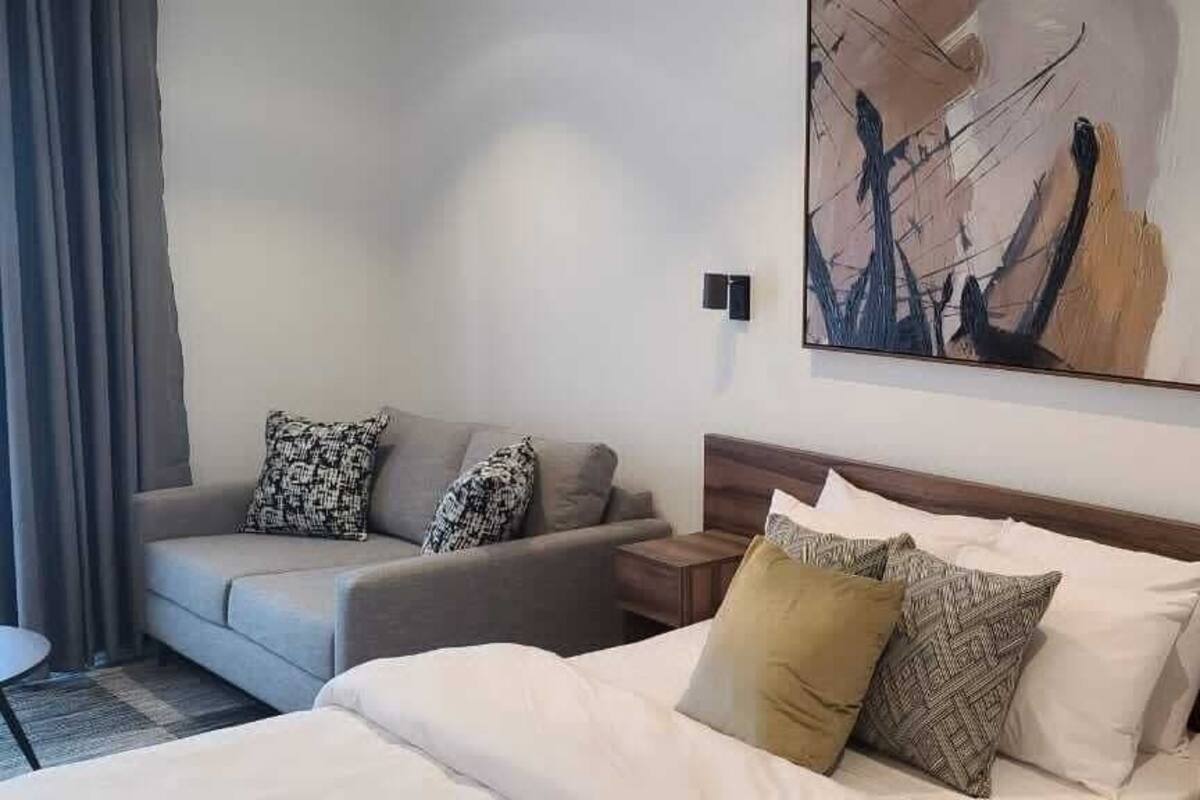 Habitación de hotel con cama, sofá, mesita de noche y un cuadro en la pared.