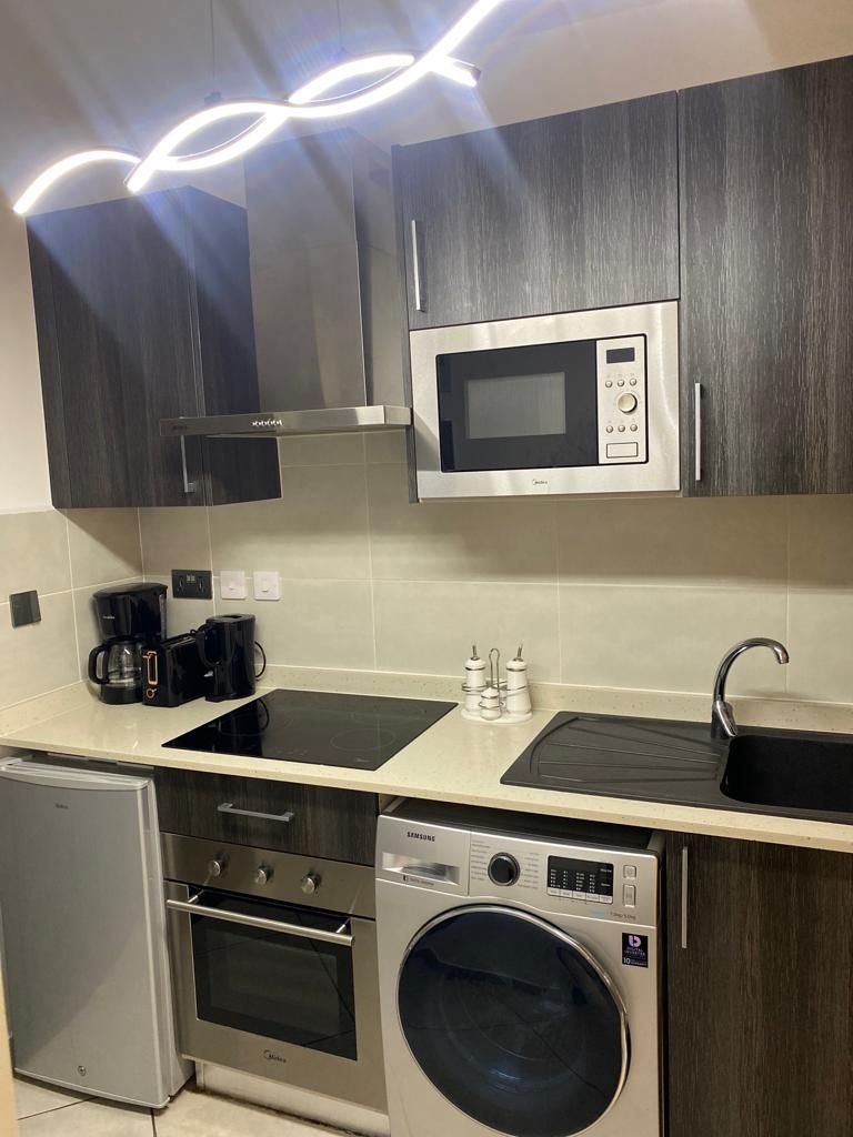 Een kleine keuken met een magnetron, koffiezetapparaat en wasmachine.