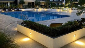 Un hotel moderno con piscina central, varios balcones y zonas exteriores bien iluminadas.