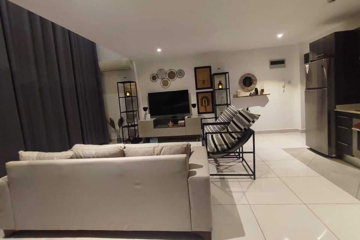 Una sala de estar moderna con un sofá, un televisor y una zona de cocina con armarios y un refrigerador.