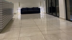 Un lobby espacioso con diseño moderno, que incluye un sofá de color oscuro, un mostrador de recepción y una entrada con puerta de vidrio.