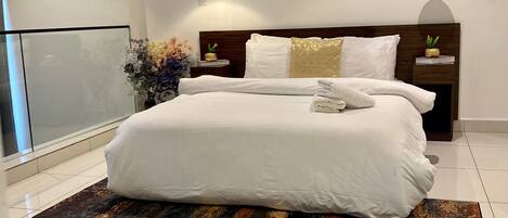 A modern bedroom with a large bed, a blue abstract rug, a framed artwork on the wall, and a nightstand with a pineapple decoration.