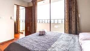Habitación de hotel con cama, ventana con cortinas estampadas y vista de la ciudad.