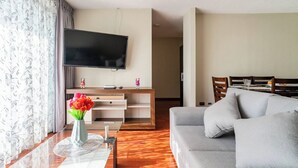 Una sala de estar moderna con una televisión de pantalla plana, un sofá, una mesa de comedor y un florero con flores.