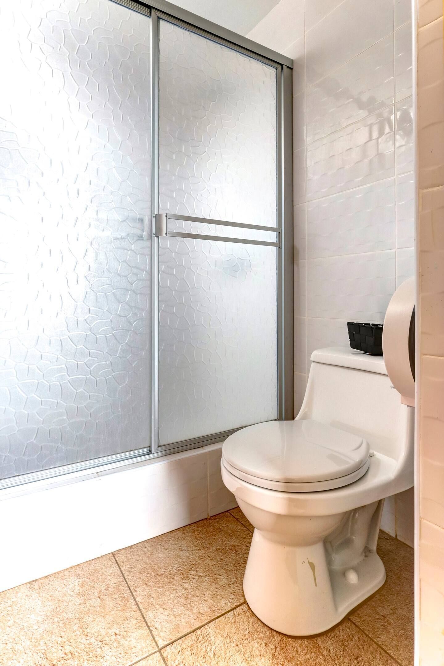 A bathroom with a white toilet, a glass shower enclosure, and a tiled floor.