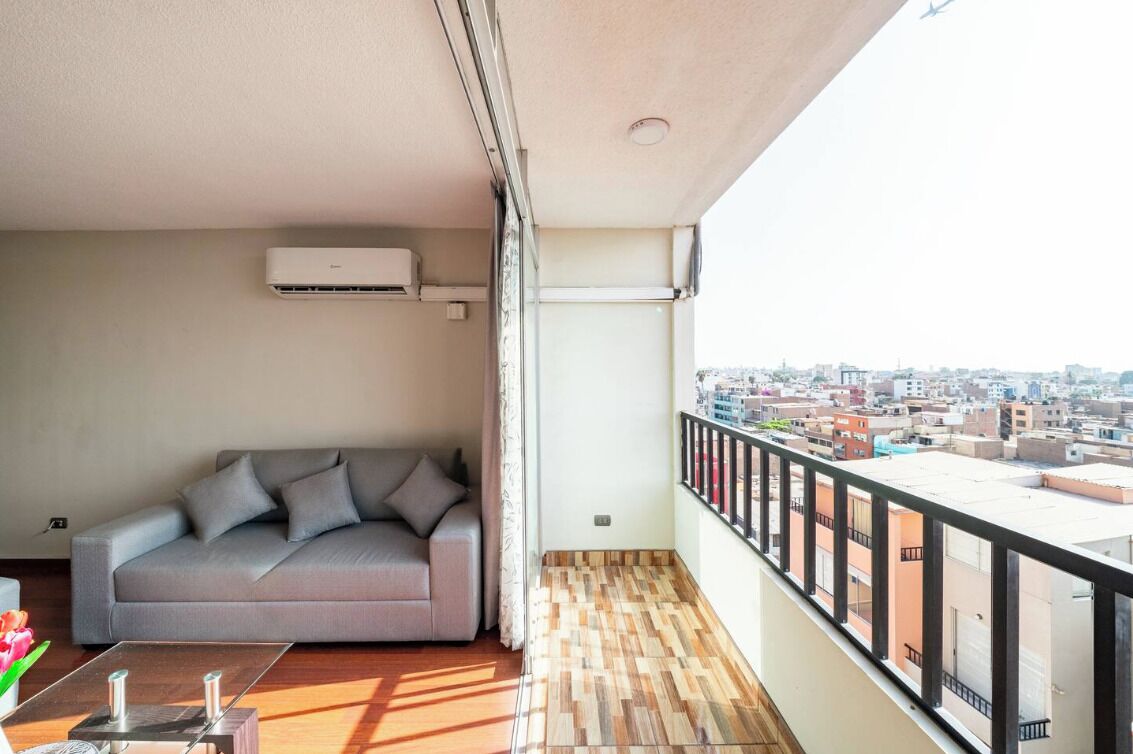 A balcony with a sofa, a wooden floor, and a city view.