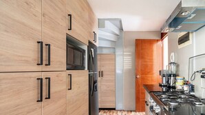 Una cocina moderna con armarios de madera, microondas integrado, refrigerador y estufa a gas.