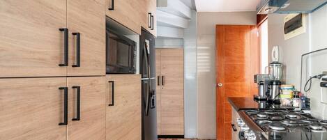 Una cocina moderna con armarios de madera, microondas integrado, refrigerador y estufa a gas.