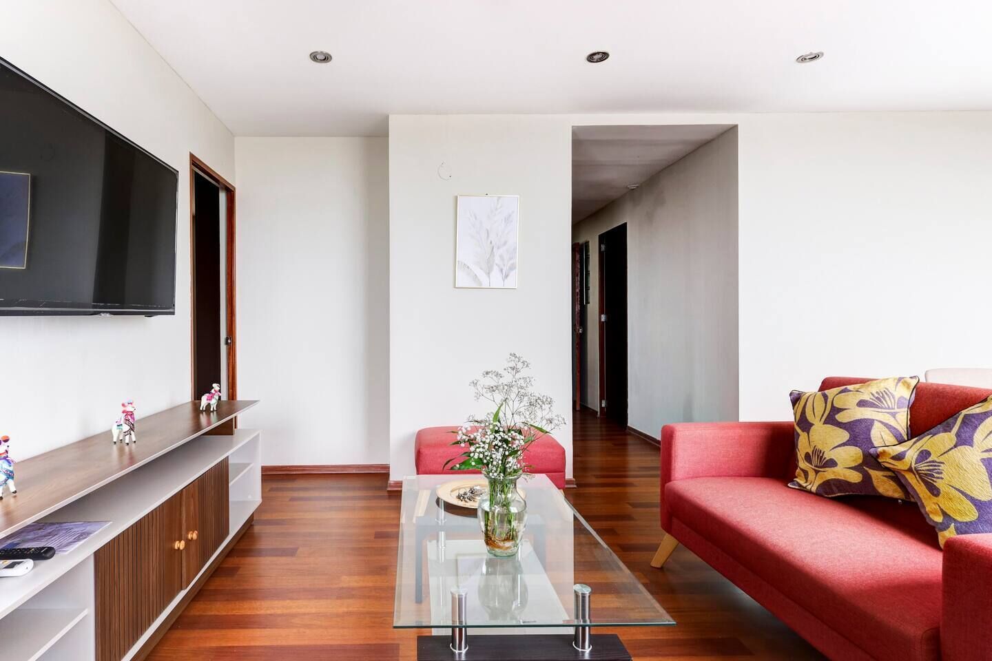 Een moderne woonkamer met een flatscreen televisie, een glazen salontafel, een rode bank en een houten kast.