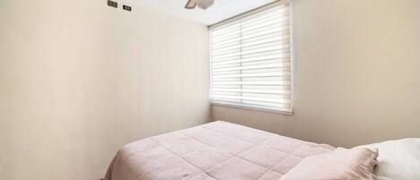 A bedroom with a bed, a ceiling fan, and a window with blinds.