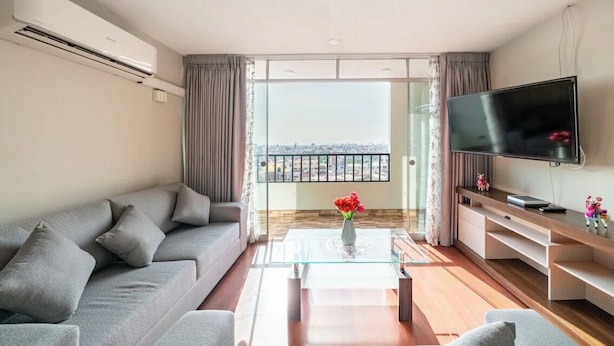 Una sala de estar moderna con un sofá gris, una mesa de centro de vidrio, un televisor de pantalla plana y un balcón con vistas.