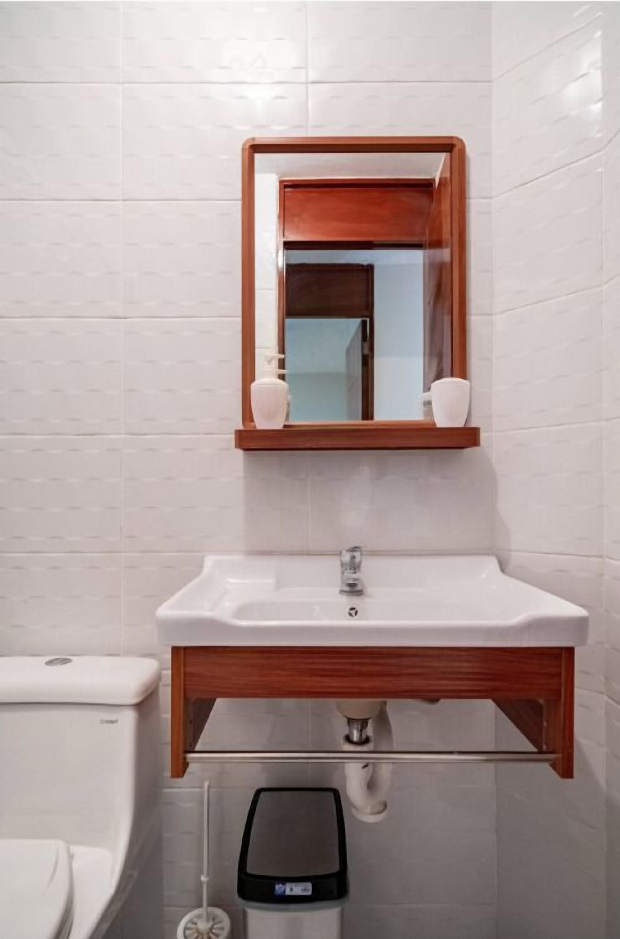 Un baño con un lavamanos blanco, tocador de madera y un espejo encima.
