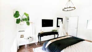 Een slaapkamer met een bed, een dressoir, een bureau, een stoel, een plant en een kroonluchter.