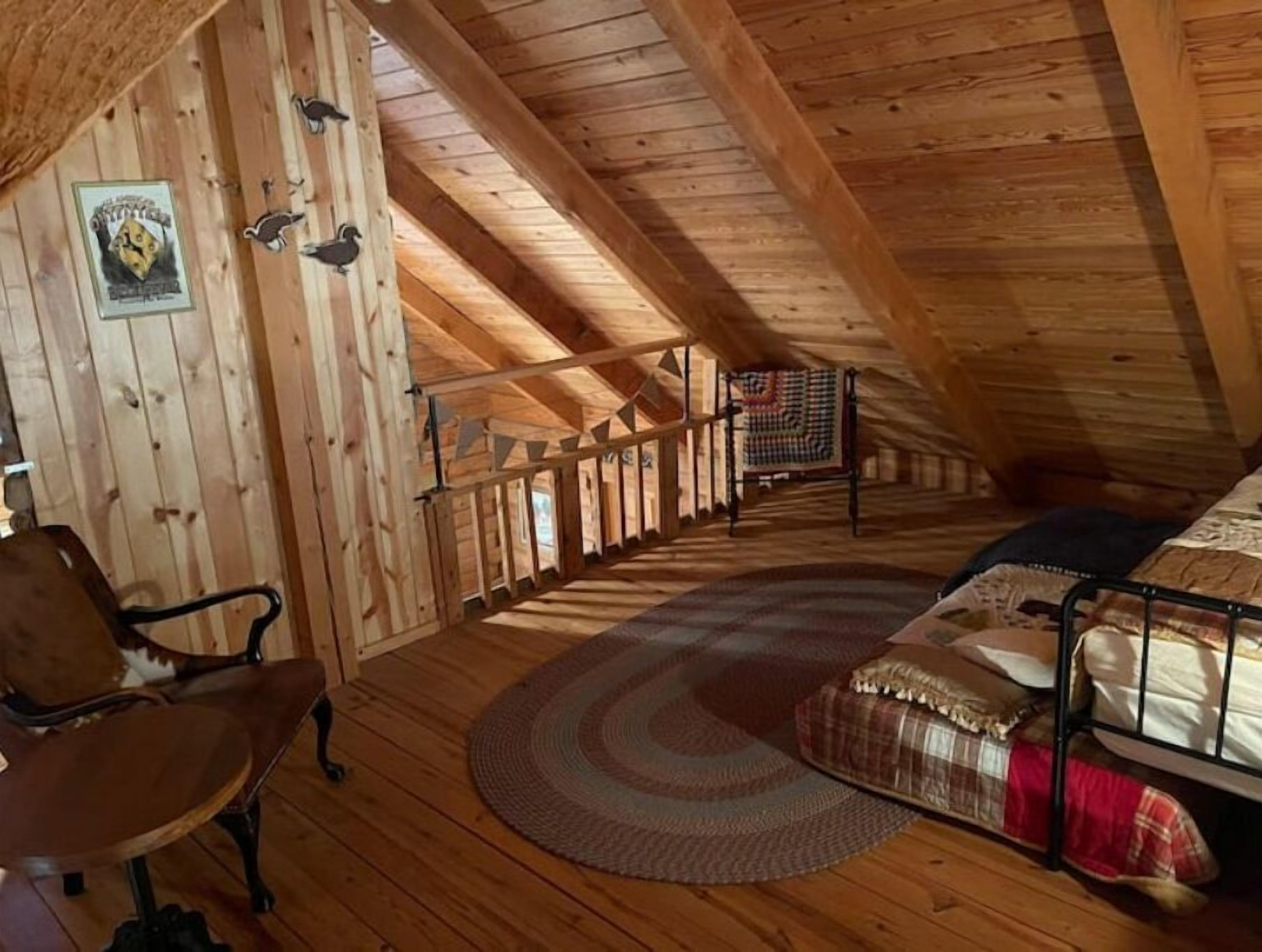 A cozy attic bedroom with wooden beams, a bunk bed, a round rug, and a chair.