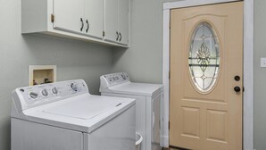 A laundry room with two front-loading washing machines, a cabinet above, and a door with a decorative glass panel.
