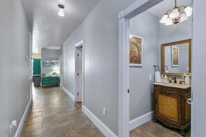 A hallway with a wooden floor, a door leading to a bathroom, and a light fixture above. - Lakefront House w/ Deck & Fire Pit (Vicksburg)