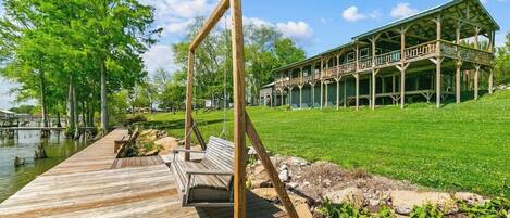 A wooden deck with a swing, a covered porch, and a building with a green roof.