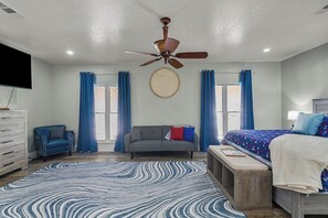 A bedroom with a bed, a ceiling fan, a sofa, a TV, and a window with curtains. - Lakefront House w/ Deck & Fire Pit (Vicksburg)