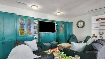 A living room with teal cabinets, a flat-screen TV, a clock, and a fish-themed wall decoration.