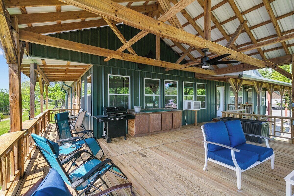 An outdoor deck with wooden furniture, a grill, and a covered area with windows.