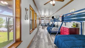 A narrow corridor with bunk beds and a ceiling fan, leading to a room with a window and a red dresser.