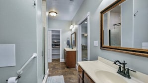 A bathroom with a vanity, sink, mirror, towel rack, and a shower area.