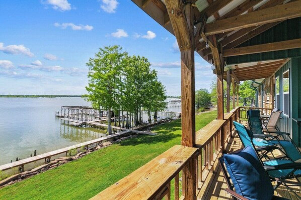 A wooden deck with outdoor seating overlooking a lake and dock.