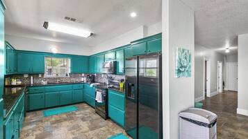 A modern kitchen with teal cabinets, stainless steel appliances, and a tiled backsplash.