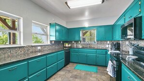 A kitchen with teal cabinets, a tiled backsplash, and a stone floor.