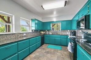 A kitchen with teal cabinets, a tiled backsplash, and a stone floor. - Lakefront House w/ Deck & Fire Pit (Vicksburg)