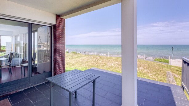 Un balcón con vista al mar, una puerta de cristal que da a una habitación y una pequeña mesa.