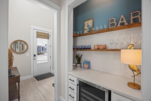 Une cuisine avec un plan de travail blanc, une étagère en bois ornée d’objets décoratifs et un panneau indiquant « BAR » au-dessus.
