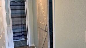A hallway with a striped shower curtain, a wooden door, and a rug.