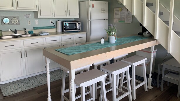A kitchen with white cabinets, a microwave, a refrigerator, and a wooden bar with stools.