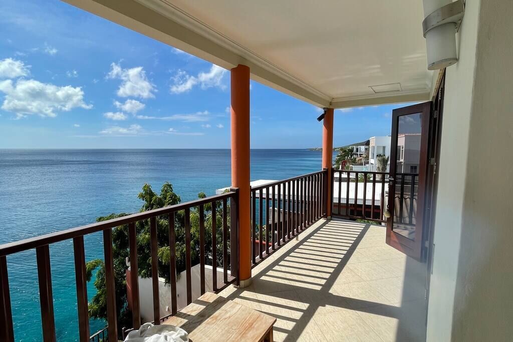 A balcony with a view of the ocean, a railing, and a door.