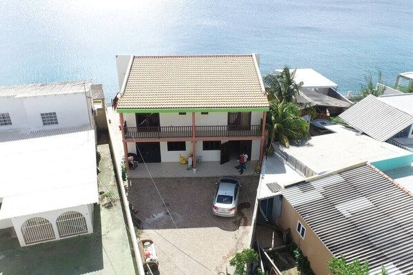 A two-story building with a tiled roof, a covered parking area, and a view of the sea.