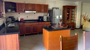 A kitchen with wooden cabinets, a black countertop, a refrigerator, and a microwave. - Villa at Playa Lagun Private Beach Curaçao (Curaçao)