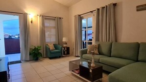 Un salon avec un canapé vert, un fauteuil turquoise, une table basse et une plante en pot.