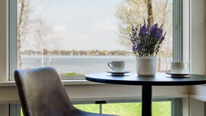 A chair and a table by a window with a view of a lake and trees.
