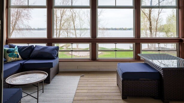 A sunroom with large windows, a sofa, a table, and a wicker chair.