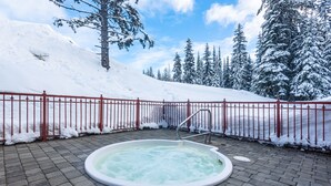 Ein Whirlpool, umgeben von einem roten Zaun, mit schneebedeckten Bäumen und blauem Himmel im Hintergrund.