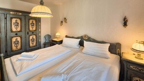 A double bed with white linens, two bedside tables with lamps, a decorative wall with floral patterns, and a ceiling light fixture.