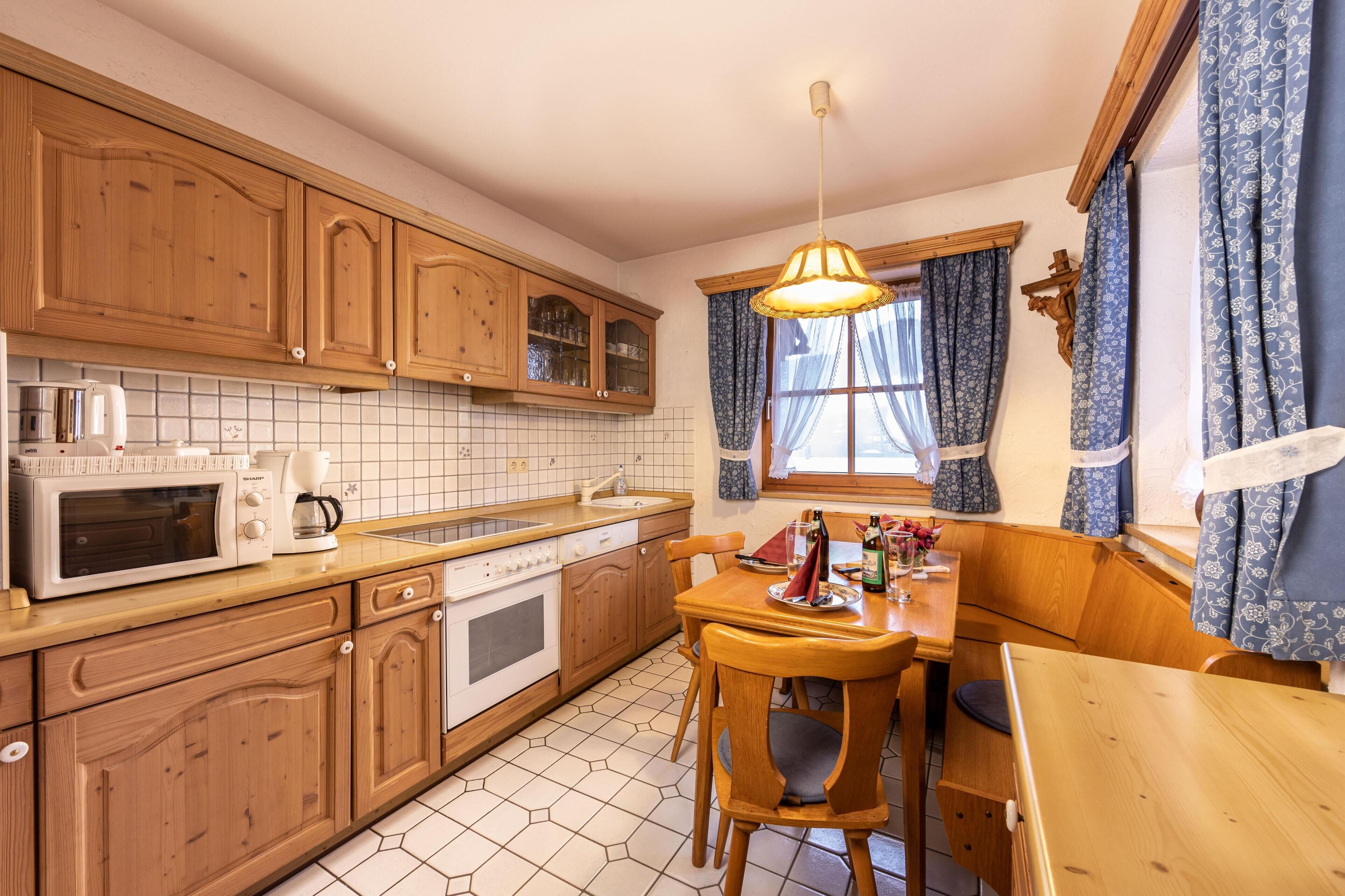 Una cocina con armarios de madera, microondas, lavaplatos y un comedor con mesa y sillas.