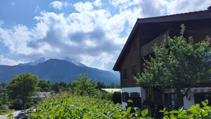A building with a sloped roof, surrounded by lush greenery and a mountain in the background.