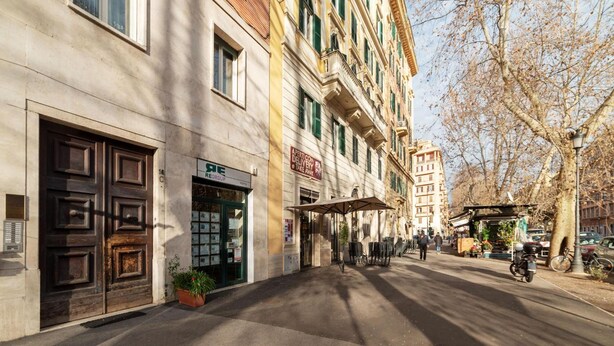 A street view of a building with a large wooden door, a sign for 'Regroup', and a small kiosk with a sign that reads 'APERTURE DELIVERY & TAKE AWAY'. - Saint Peter View - Saint Peter View 2 pax (Rome)