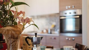 A kitchen with a coffee maker, a cup, and a vase with flowers on a table. - Saint Peter View - Saint Peter View 2 pax (Rome)