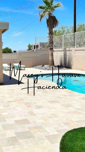 Zona de piscina con una palmera, una cerca y un edificio al fondo.