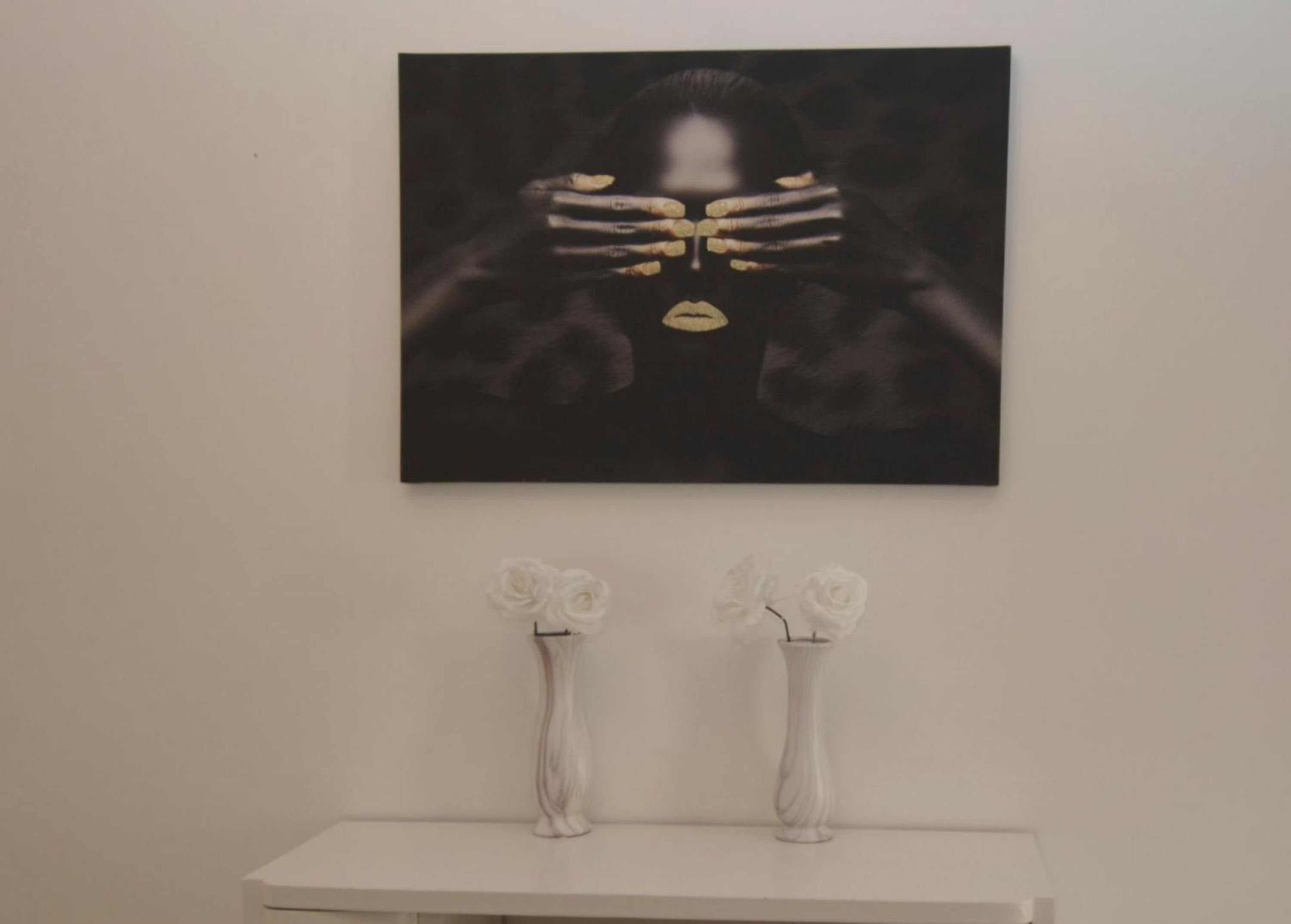 A painting of a woman with a blurred face, two white vases with flowers, and a white table below.
