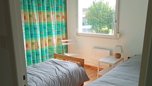 A bedroom with two beds, a window with a view of greenery, a white chair, and a table. - Quiet, bright house (Wissant)